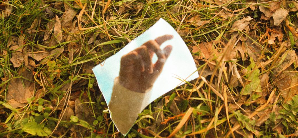 Shard of broken mirror on grass reflects womans hand